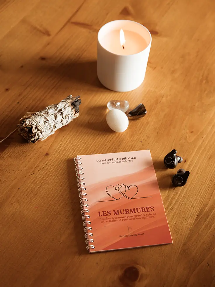 Livret audio posé sur une table en bois avec bougie allumée, sauge, pierres et écouteurs - produit en vente sur Toujours L, site de rituels bien-être pour femme aidante d'une proche atteinte de cancer