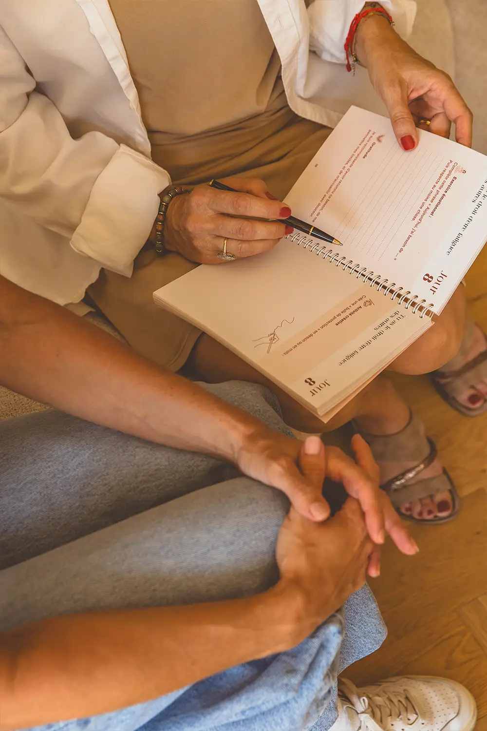 Deux femmes assises se tenant la main, l'une écrivant dans un carnet ouvert sur ses genoux - collection Aidantes en vente sur Toujours L, site pour femme aidante d'une proche atteinte de cancer