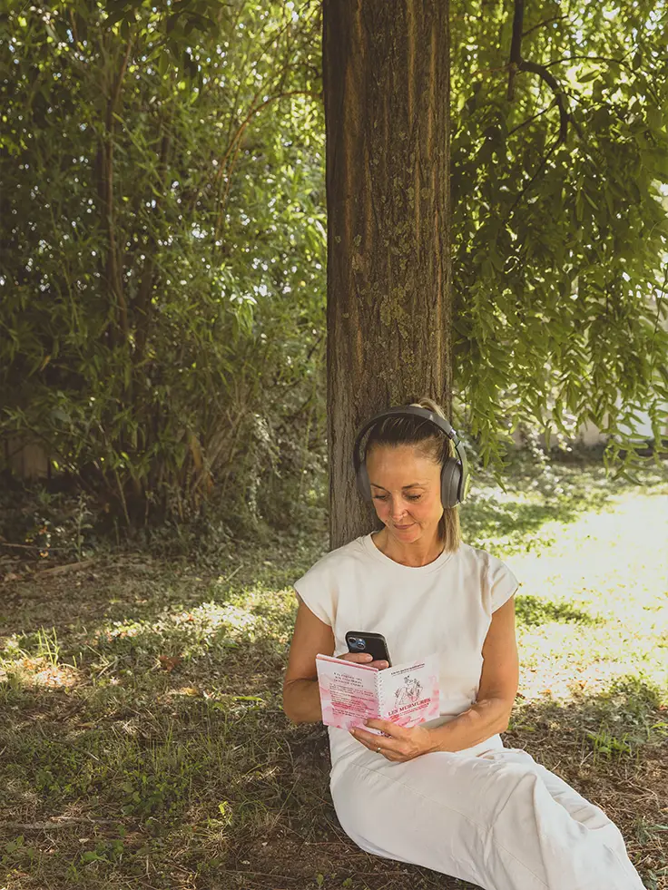 Femme au casque assise sous un arbre, lisant un livret rose Les Murmures - collection Rémission en vente sur Toujours L, site pour femme après un cancer