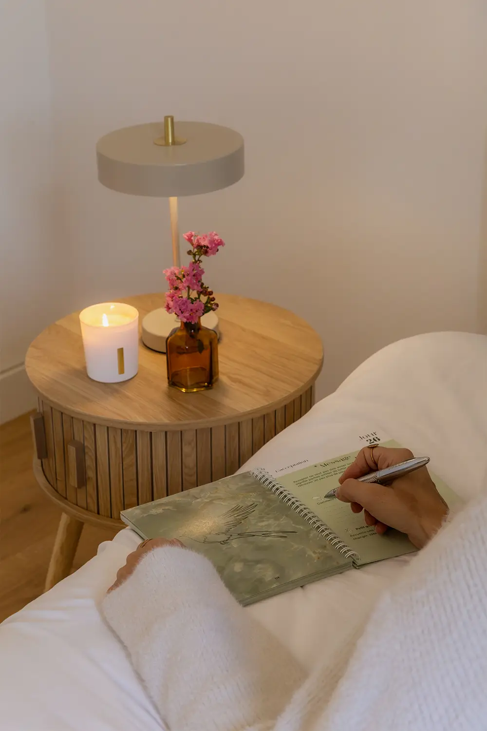 Carnet vert ouvert sur un canapé, avec bougie allumée et fleurs sur une table de chevet - collection Rémission en vente sur Toujours L, site pour femme après un cancer