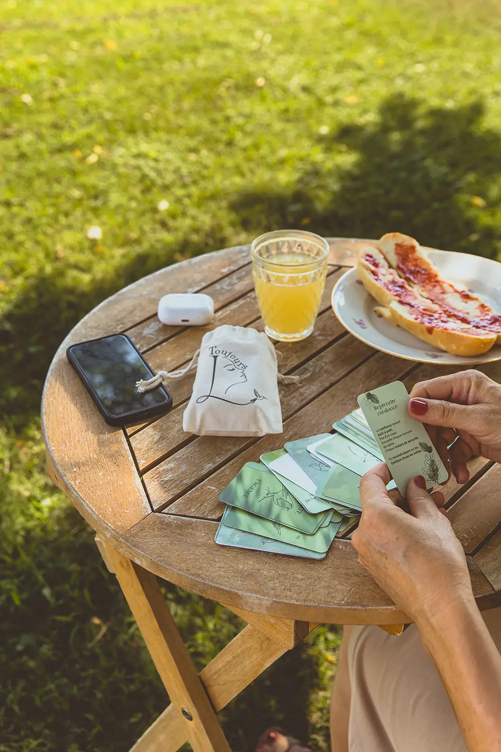Femme triant des cartes vertes sur une table de jardin, avec pochette en coton, écouteurs et tartine - collection Rémission en vente sur Toujours L, site pour femme après un cancer